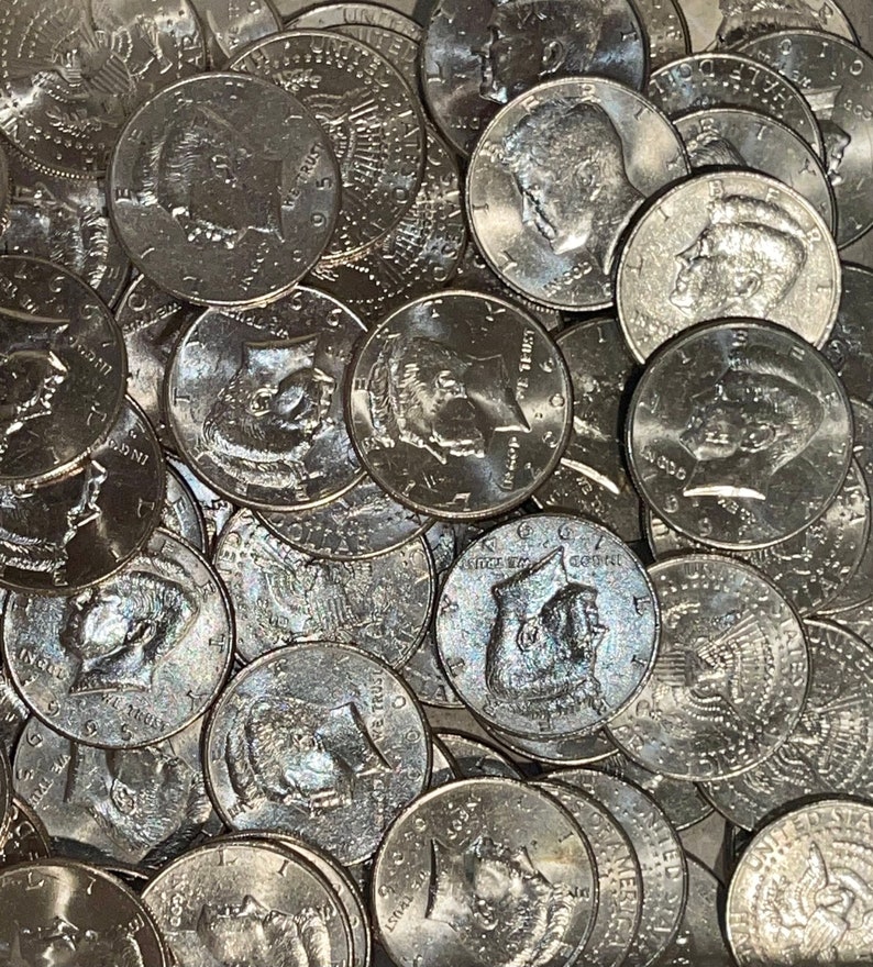 May include: A close-up shot of a pile of silver half-dollar coins. The coins feature the profile of a man on one side and an eagle on the other. The coins are scattered, with some partially visible.