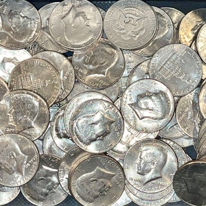 May include: A collection of silver Kennedy half-dollar coins, many of which are dated 1976. The coins are in a dark container. The coins feature the profile of John F. Kennedy and the image of Independence Hall.