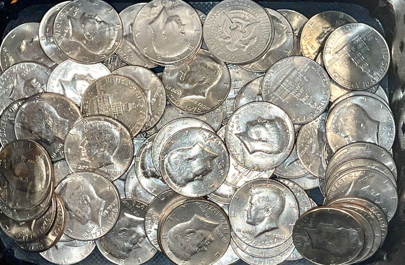 May include: A collection of silver Kennedy half-dollar coins, many of which are dated 1976. The coins are in a dark container. The coins feature the profile of John F. Kennedy and the image of Independence Hall.