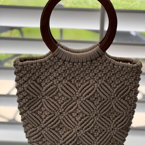 Puede incluir: Un bolso de mano de crochet beige con un asa de madera marr&oacute;n.