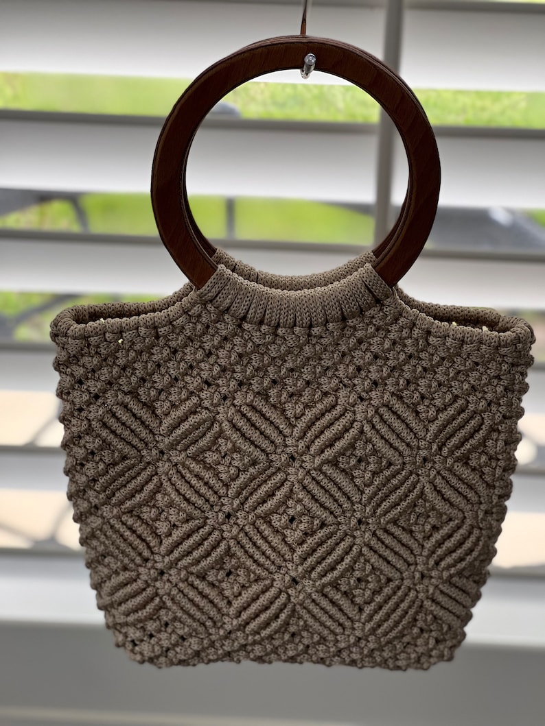 Puede incluir: Un bolso de mano de crochet beige con un asa de madera marr&oacute;n.