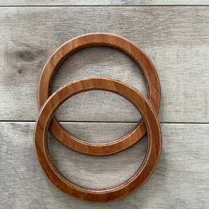 Puede incluir: Dos aros de bordado de madera, uno encajado dentro del otro. Los aros son de color marr&oacute;n y tienen un acabado de madera natural.