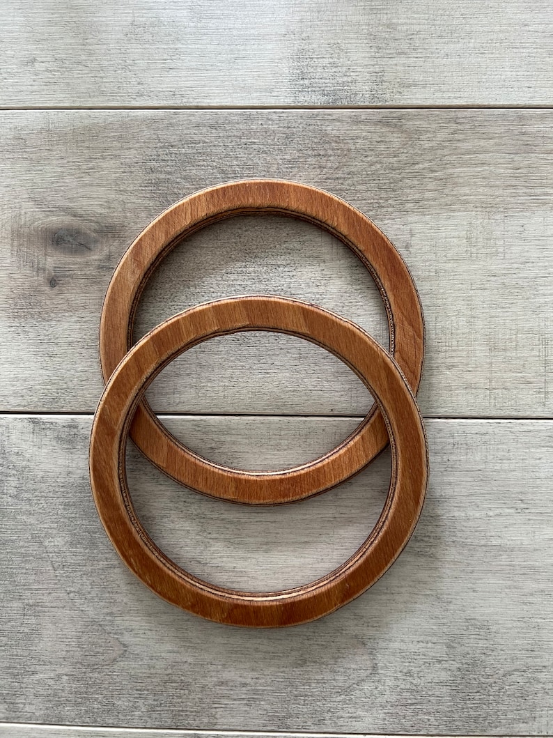 Puede incluir: Dos aros de bordado de madera, uno encajado dentro del otro. Los aros son de color marr&oacute;n y tienen un acabado de madera natural.