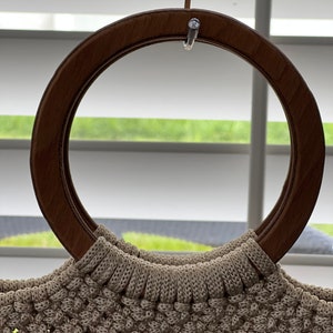 Puede incluir: Un bolso de mano de crochet beige con un asa de madera marr&oacute;n.