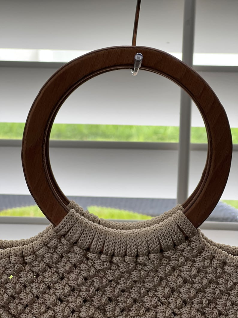 Puede incluir: Un bolso de mano de crochet beige con un asa de madera marr&oacute;n.