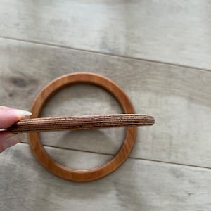 Puede incluir: Un anillo de madera con un acabado de madera natural. El anillo est&aacute; hecho de m&uacute;ltiples capas de madera, creando un patr&oacute;n a rayas.