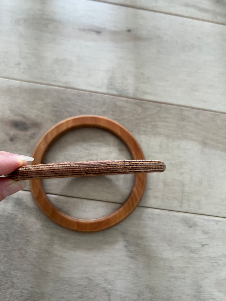 Puede incluir: Un anillo de madera con un acabado de madera natural. El anillo est&aacute; hecho de m&uacute;ltiples capas de madera, creando un patr&oacute;n a rayas.