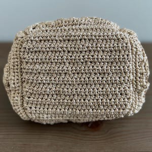 Pu&ograve; includere: Un primo piano di una borsa in crochet beige. La borsa &egrave; realizzata con un filato fine e testurizzato e ha una superficie liscia e uniforme.