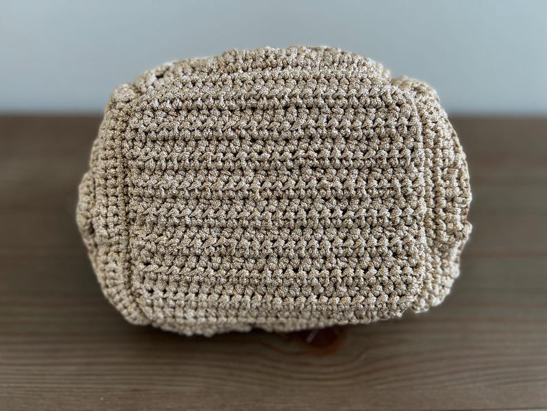 Pu&ograve; includere: Un primo piano di una borsa in crochet beige. La borsa &egrave; realizzata con un filato fine e testurizzato e ha una superficie liscia e uniforme.