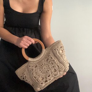 Pu&ograve; includere: Una borsa a mano in crochet beige con manico in legno. La borsa ha un design delicato e traforato, perfetta per portare con s&eacute; gli oggetti essenziali di tutti i giorni.