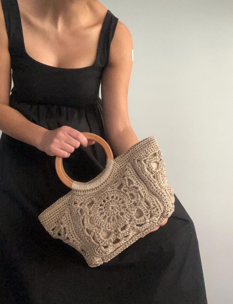 Pu&ograve; includere: Una borsa a mano in crochet beige con manico in legno. La borsa ha un design delicato e traforato, perfetta per portare con s&eacute; gli oggetti essenziali di tutti i giorni.