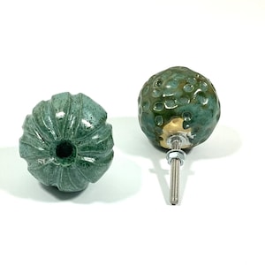 Può includere: Due pomelli per armadi in ceramica in uno schema di colori verde e marrone. Un pomello ha una superficie testurizzata e irregolare, mentre l'altro ha una superficie liscia e rigata.