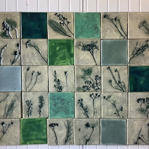 Puede incluir: Una pared cubierta con 16 azulejos cuadrados, cada uno con una ilustración botánica diferente en tonos de verde y gris. Los azulejos están dispuestos en una cuadrícula.