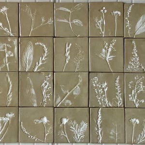 Könnte beinhalten: Vierundzwanzig quadratische Fliesen mit hellbraunem Hintergrund und weißen gepressten Pflanzen. Die Fliesen sind in vier Reihen mit jeweils sechs Fliesen angeordnet.
