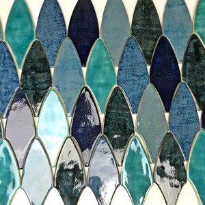 May include: A sheet of ceramic mosaic tiles in various shades of blue and green. The tiles are shaped like elongated teardrops and arranged in a staggered pattern.