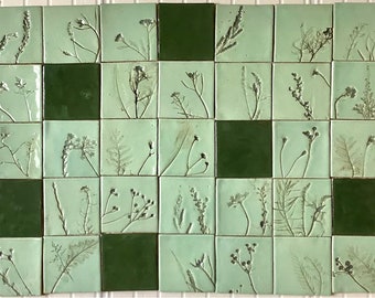 May include: A wall covered in green and white square tiles. Each tile features a different pressed botanical design.