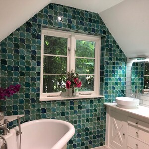 May include: A bathroom with a white clawfoot tub, two white sinks, and a green and blue mosaic tile wall. The wall is decorated with a green and blue fish scale pattern. The bathroom has a white tiled wall with a white trim.