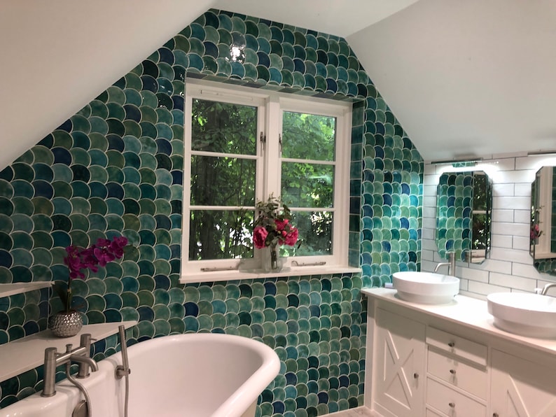 May include: A bathroom with a white clawfoot tub, two white sinks, and a green and blue mosaic tile wall. The wall is decorated with a green and blue fish scale pattern. The bathroom has a white tiled wall with a white trim.