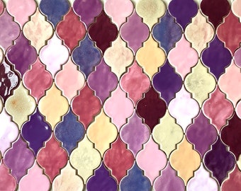 May include: A wall tiled with a geometric pattern of small, colorful, iridescent tiles. The tiles are shaped like quatrefoils and are arranged in a staggered pattern. The colors of the tiles are shades of purple, pink, and yellow.