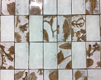 May include: A white tile wall with brown leaf patterns. The tiles are arranged in a grid pattern.