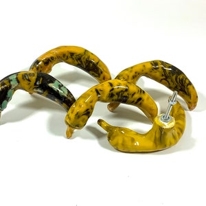 Peut inclure: Quatre poignées de tiroir en céramique jaune en forme de poivron avec des marbrures noires et bleues. Les poignées sont munies d'une fixation à vis.