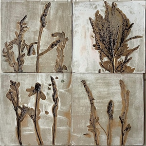 May include: Set of four square ceramic tiles with pressed botanicals. Each tile features a different type of dried plant, including grasses and flowers, in shades of brown and gold against a light beige background.