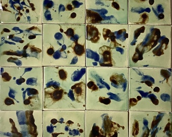 May include: A set of 16 ceramic tiles with a green background and abstract blue and brown splatter paint design.