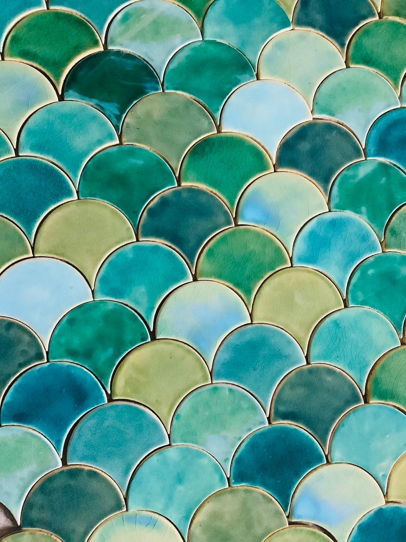 May include: A close-up of a wall covered in green, blue, and teal ceramic tiles. The tiles are arranged in a fish scale pattern.