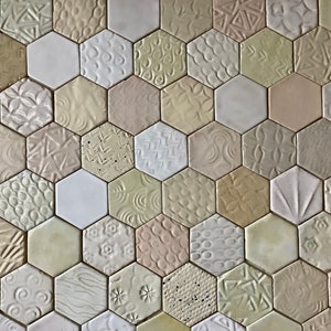 Könnte beinhalten: Nahaufnahme einer Wand, die mit sechseckigen Fliesen bedeckt ist. Die Fliesen sind aus Keramik und haben eine Vielzahl von geprägten Mustern und Texturen. Die Fliesen sind in Weiß-, Creme- und Beigetönen gehalten.