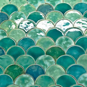 May include: A close-up of a wall covered in green and blue iridescent ceramic tiles. The tiles are arranged in a fish scale pattern.