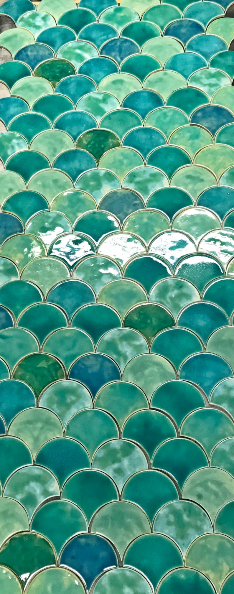 May include: A close-up of a wall covered in green and blue iridescent ceramic tiles. The tiles are arranged in a fish scale pattern.