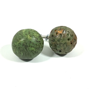 Puede incluir: Dos pomos de armario de cerámica verde con una superficie texturizada. Un pomo tiene una superficie lisa y el otro tiene una superficie texturizada con pequeños agujeros.