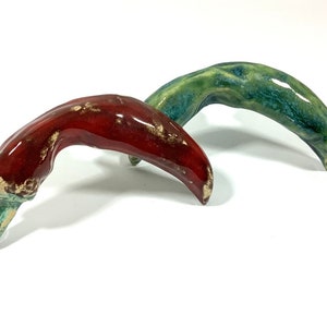 Könnte beinhalten: Zwei Keramik-Chili-Pfeffer-Figuren, eine rot und eine grün, mit rustikalem, glasiertem Finish.