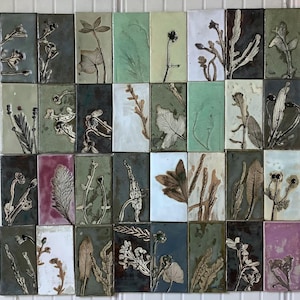 May include: A collection of 24 ceramic tiles with various botanical designs. Each tile features a different pressed plant, flower, or leaf in shades of green, brown, white, and pink.