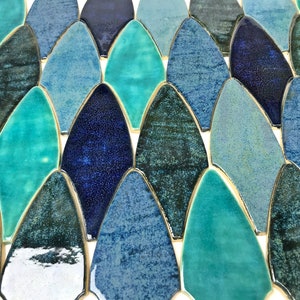 May include: A close-up of a mosaic tile sheet featuring a variety of blue and green iridescent ceramic tiles in a fish scale pattern.