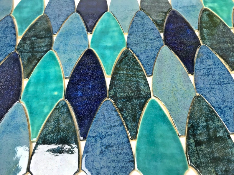 May include: A close-up of a mosaic tile sheet featuring a variety of blue and green iridescent ceramic tiles in a fish scale pattern.