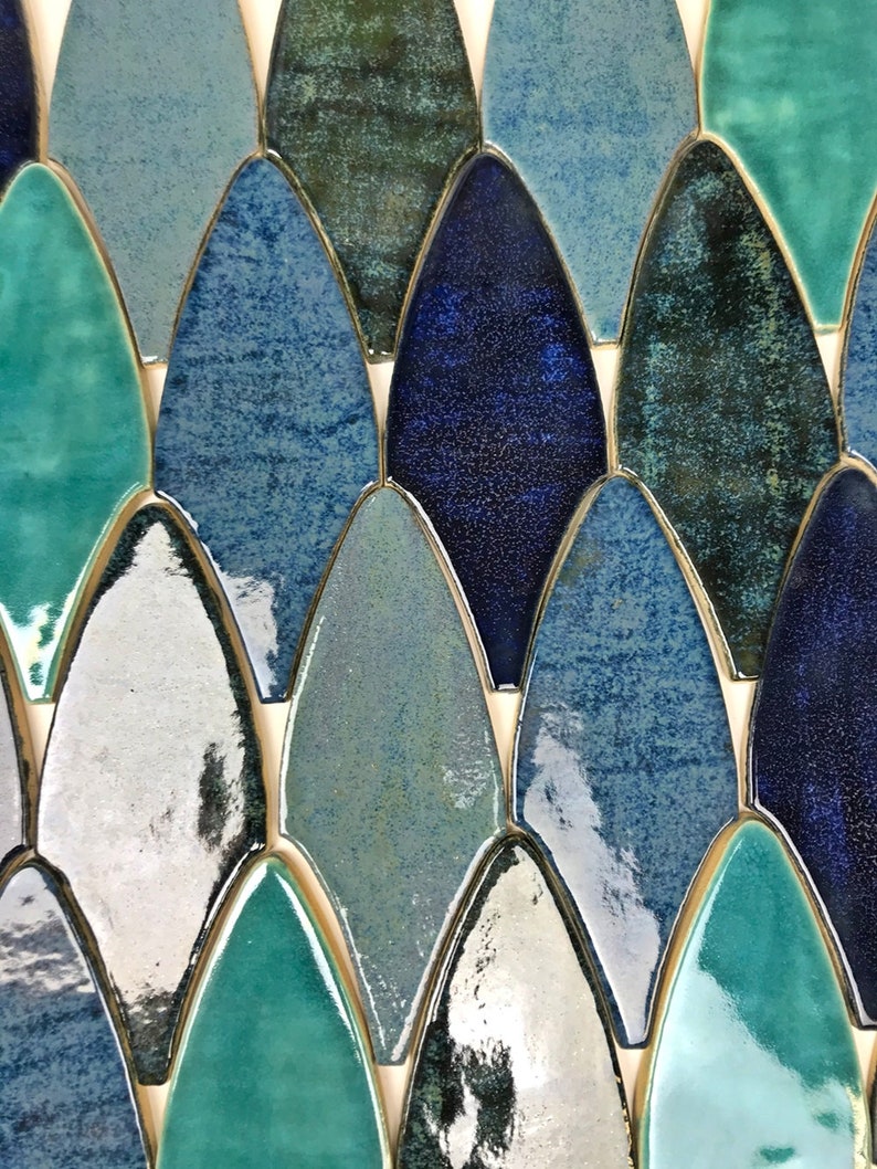 May include: A close-up of a mosaic tile sheet featuring a variety of blue, green, and white glazed ceramic tiles in a fish scale pattern.