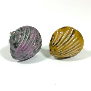 May include: Two ceramic seashell drawer pulls, one in a purple and green glaze and the other in a yellow glaze.