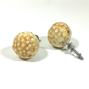 Può includere: Due pomelli per porte in ceramica a forma di palla da golf con un motivo maculato marrone e bianco. Il pomo a destra ha una vite e una rondella argentate.