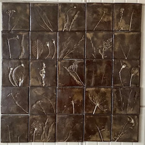 May include: A collection of 25 square ceramic tiles arranged in a grid. Each tile features a pressed botanical design in shades of brown and white. The botanical elements include leaves, stems, and flowers, creating a natural, earthy aesthetic.
