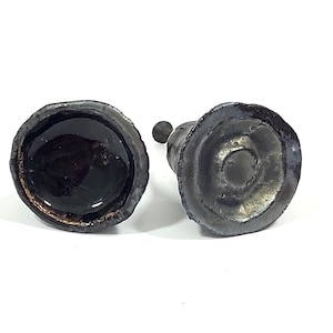 Könnte beinhalten: Zwei schwarze Keramik-Flaschenverschlüsse mit einem einzigartigen Design. Ein Verschluss hat eine glatte, glänzende Oberfläche, während der andere eine strukturierte, matte Oberfläche hat.