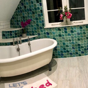May include: A white clawfoot bathtub with silver fixtures in a bathroom with white subway tile, green mosaic tile, and a white vanity with two sinks.