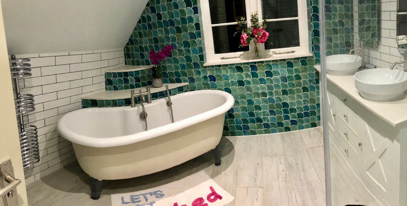 May include: A white clawfoot bathtub with silver fixtures in a bathroom with white subway tile, green mosaic tile, and a white vanity with two sinks.