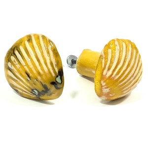 Peut inclure: Deux boutons de cabinet en céramique jaune en forme de coquillages avec des détails blancs et noirs.