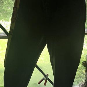 May include: Dark denim capri pants with a decorative side panel. The pants are displayed on a mannequin. The side panel has a colorful design. The pants have a button closure and pockets.