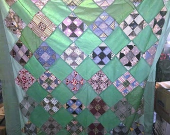 May include: A green patchwork quilt with a diamond pattern. The quilt is made of various fabrics in shades of pink, blue, white, and brown. The quilt is handmade and has a vintage look.