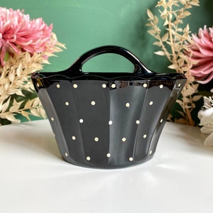 May include: A black ceramic planter with a white polka dot pattern and a handle. The planter is shaped like a basket and has a scalloped edge.
