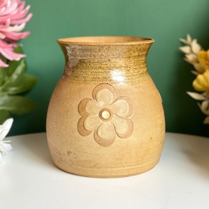 Op de afbeelding: Een bruine keramische vaas met een reliëfbloemdessin. De vaas heeft een brede opening en een rond lichaam.