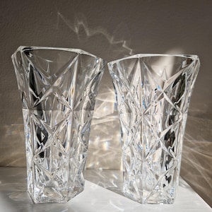 May include: Two clear glass vases with a geometric, diamond-shaped pattern. The vases are empty and sitting on a white surface.