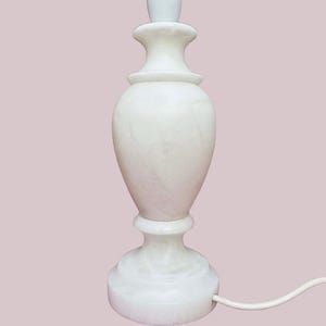 May include: A white marble table lamp with a classic urn shape. The lamp features a round base, a bulbous body, and a decorative top. The lamp is approximately 30 cm tall and has a white cord.